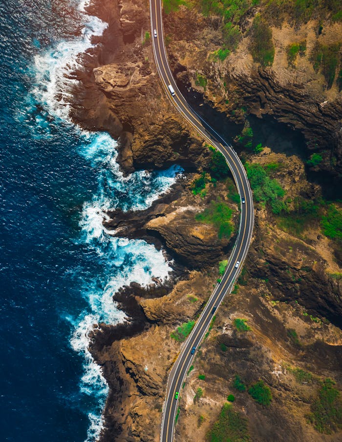 services-04 Stunning aerial shot of a winding coastal road in Hawaii with vibrant ocean waves.