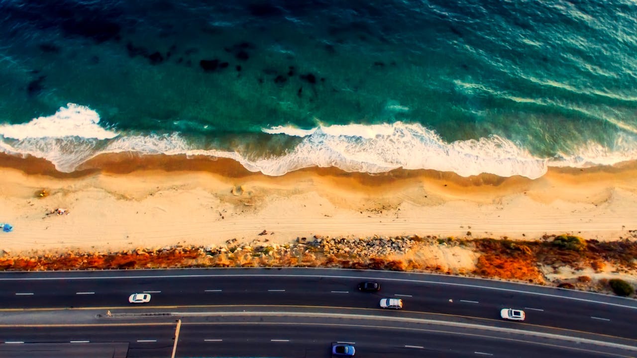 services-02 Stunning aerial view of a highway parallel to a tranquil beach and ocean waves.